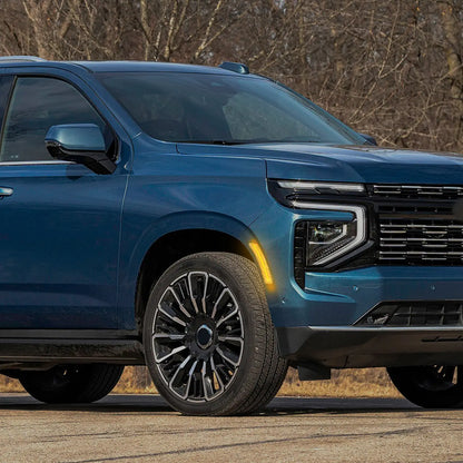 Close-up view of a blue SUV parked outdoors, highlighting the front wheel, modern alloy rim, illuminated amber side marker light, and sleek headlight design with black grille.
