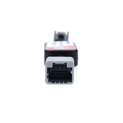 Close-up view of an automotive Idle Stop Disable Bypass device connector, showing a gray rectangular plug with multiple metal pins designed for easy vehicle system connection.