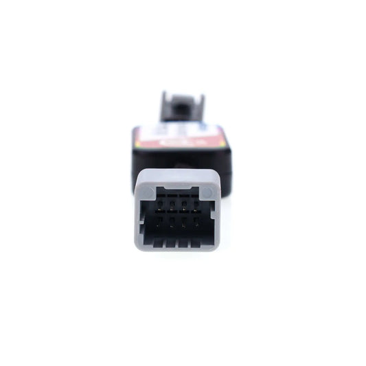 Close-up view of an automotive Idle Stop Disable Bypass device connector, showing a gray rectangular plug with multiple metal pins designed for easy vehicle system connection.