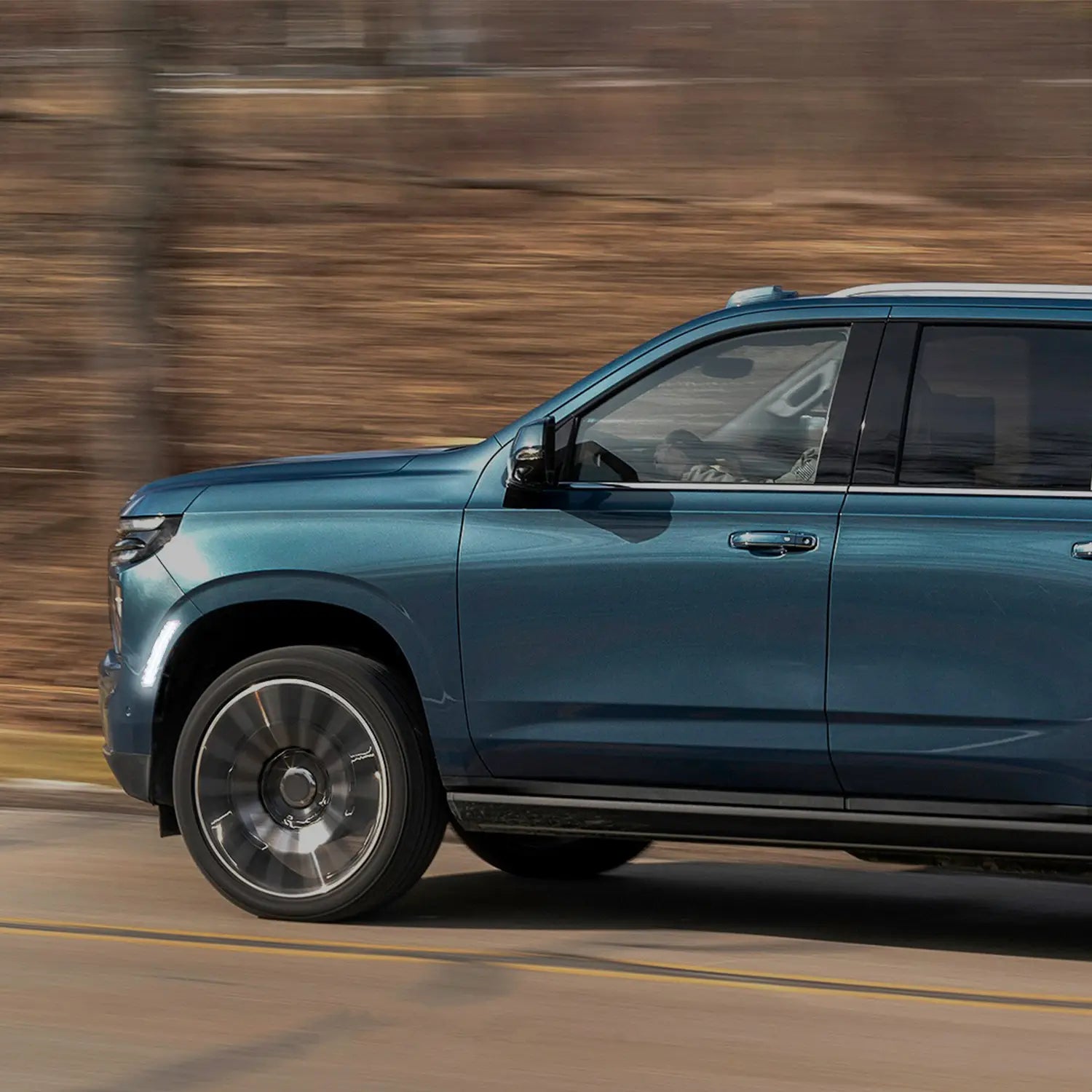 Close-up view of a blue SUV parked outdoors, highlighting the front wheel, modern alloy rim, illuminated white side marker light, and sleek headlight design with black grille.